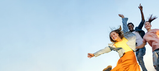 Group of young multiracial friends enjoying freedom together - Happy people jumping to blue sky background - Friendship concept - Copy space.