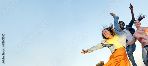 Group of young multiracial friends enjoying freedom together - Happy people jumping to blue sky background - Friendship concept - Copy space.
