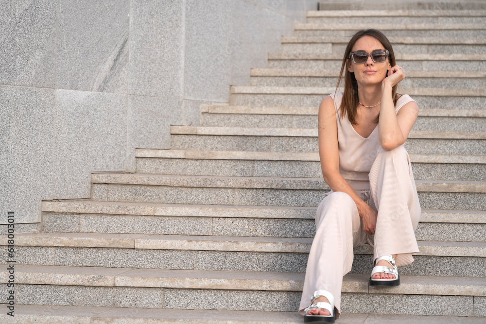 Summer urban portrait of a young woman who sits on the steps in the street. Summer urban portrait of a young woman who sits on the steps in the street.