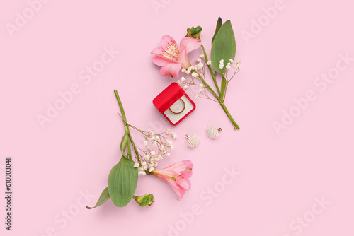 Box with wedding ring, earrings and flowers on pink background
