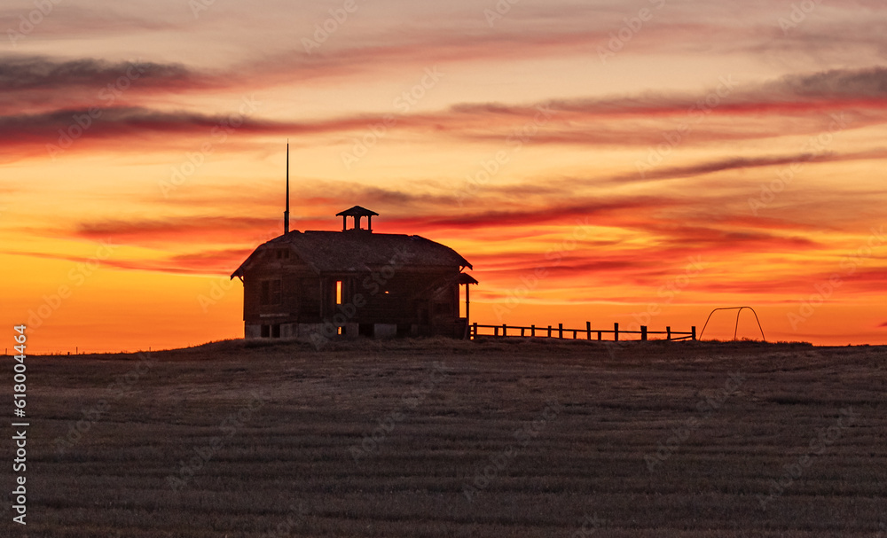 Old Abandoned Schoolhouse, with corral and swing silhouetted  in the setting sun. Wasco County, Oregon