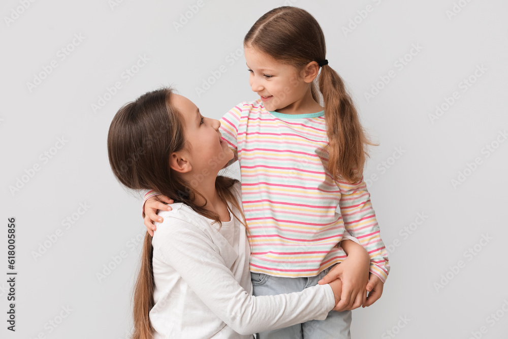Cute little sisters hugging on light background Cute little sisters hugging on light background