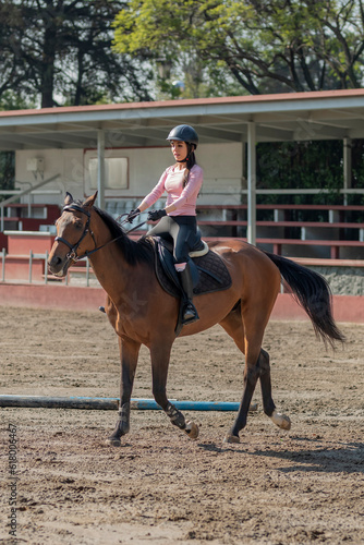 Vertical image of a young woman who is riding a horse while taking lessons in an equestrian center