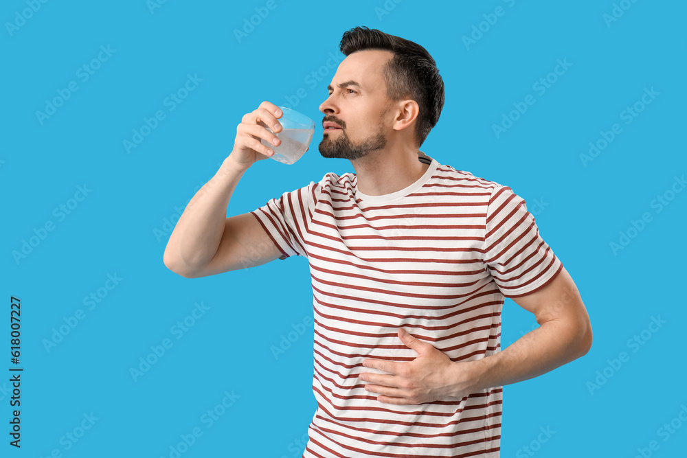 Young man drinking water with dissolved tablet on blue background Young man drinking water with dissolved tablet on blue background