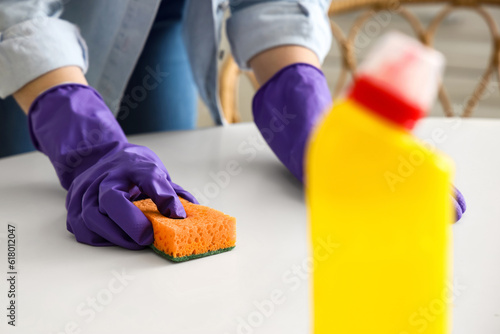 Woman in purple rubber gloves cleaning table with sponge