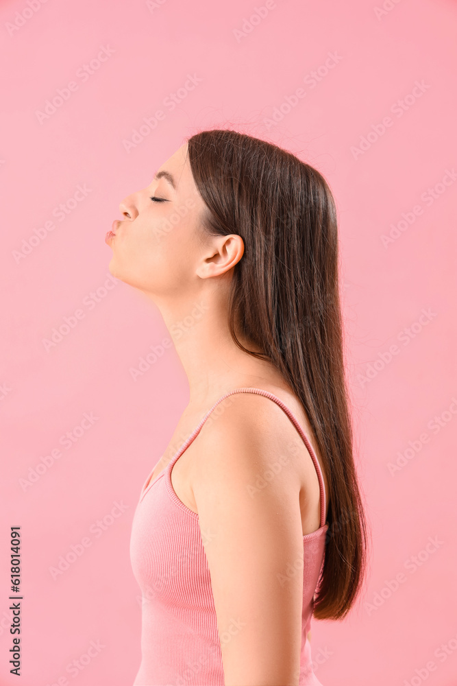 Young woman blowing kiss on pink background