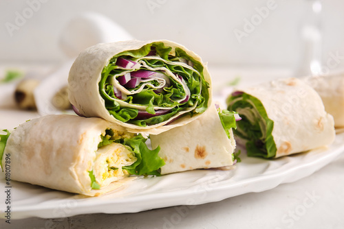 Plate of tasty lavash rolls with onion and egg on light background