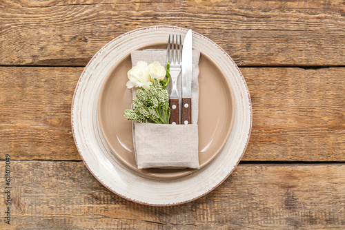 Beautiful table setting with cutlery and floral decor folded in napkin on wooden table