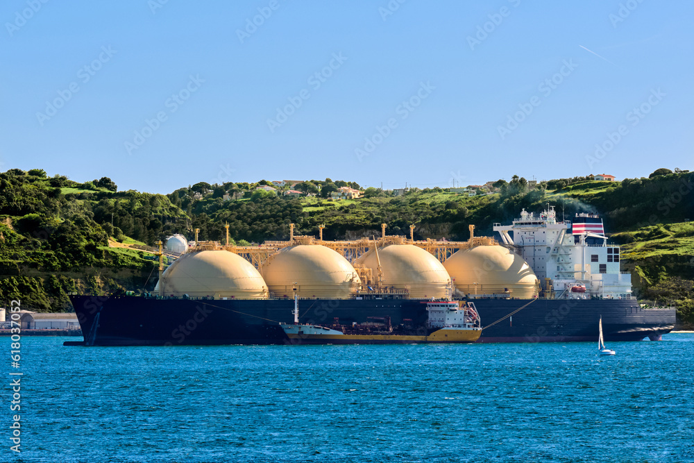 LNG tanker moored by industrial pier and green hill on sunny day