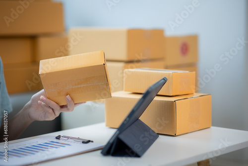 Asian young woman small business owner sitting with tablet, calculator, smartphone and box in house preparing to ship to customer, seller business concept for SME