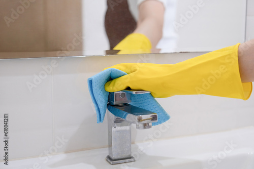 Woman, housewife wiping faucet with cloth.