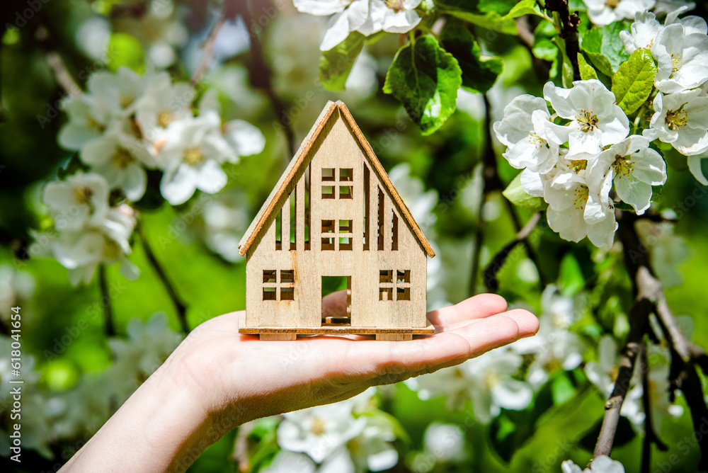 The girl holds the house symbol against the background of blossoming appletree
The girl holds the house symbol against the background of blossoming appletree