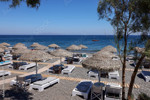 Fototapeta Naklejka Na Ścianę i Meble -   Sun loungers on the black volcanic beach of Kamari in Santorini. Cyclades, Greece
