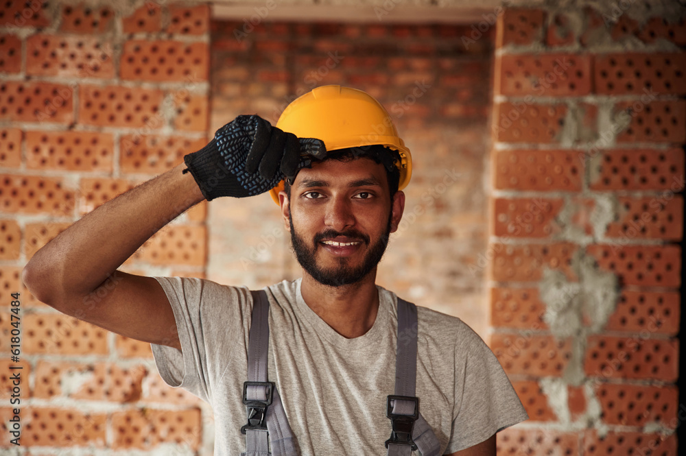 Indoors against brick wall. Handsome Indian man is on the construction site Indoors against brick wall. Handsome Indian man is on the construction site