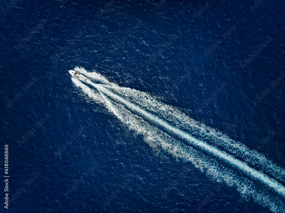 High aerial view of a motor speeboat traveling over blue ocean and leaving a trail of fom and bubbles
