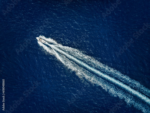 High aerial view of a motor speeboat traveling over blue ocean and leaving a trail of fom and bubbles