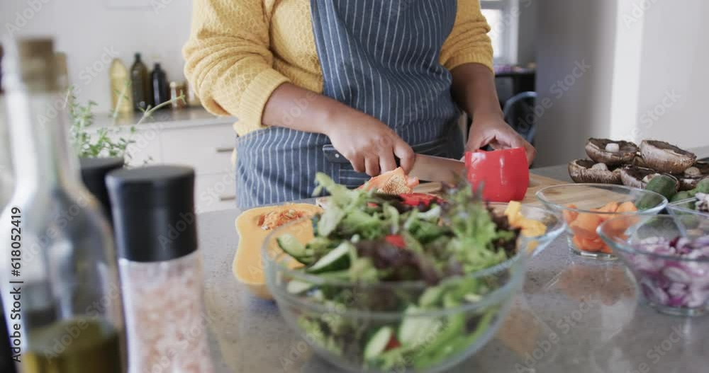 Midsection of african american woman in apron chopping vegetables in kitchen, slow motion Midsection of african american woman in apron chopping vegetables in kitchen, slow motion