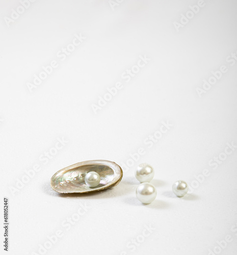 Half of a mother-of-pearl seashell with several pearls on a white background