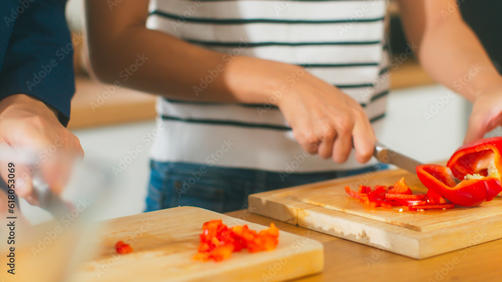 Beautiful young Asian lover hands slicing red bell pepper. Happy couple enjoy cooking together having fun in cozy kitchen using knife cutting vegetable preparing healthy food vegetarian salad