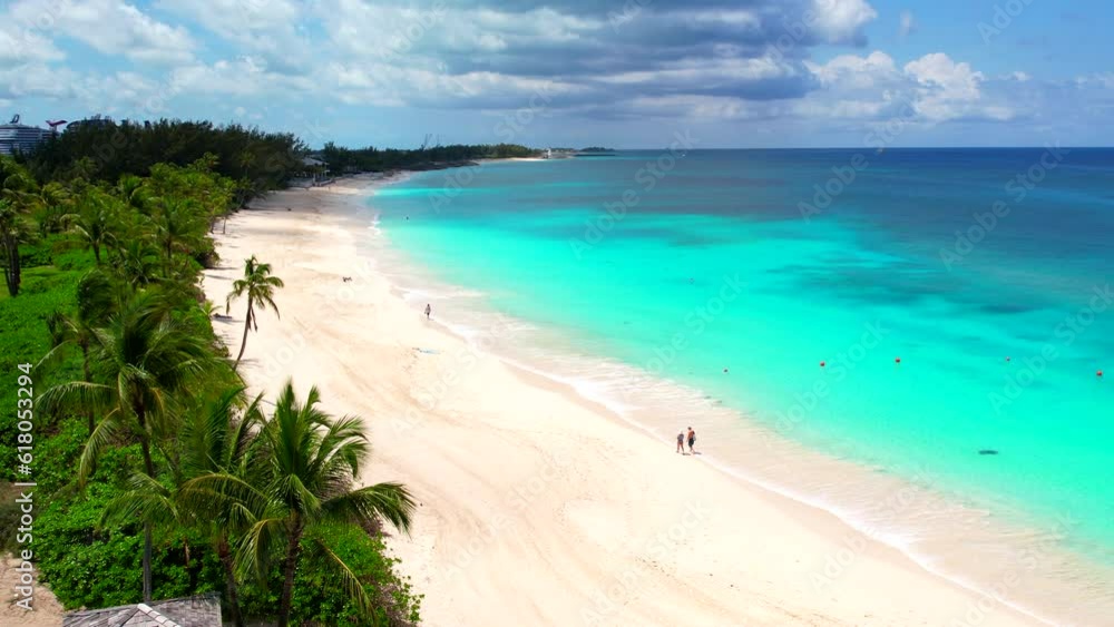 Paradise on an almost empty sea beach. Bahamas coast line. Blue water, White sand, Green palms, sunny Summer day add the Caribbean's in Atlantic ocean. Blue clouds, people walking by the beach. Paradise on an almost empty sea beach. Bahamas coast line. Blue water, White sand, Green palms, sunny Summer day add the Caribbean's in Atlantic ocean. Blue clouds, people walking by the beach.
