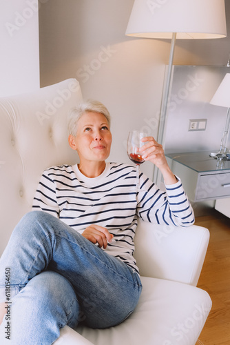 young blonde woman woman drinking red wine sitting in armchair at hotel room photo