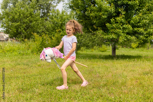 Photography beautiful little girl cowboy playing running riding on toy stick horse in park in nature on summer