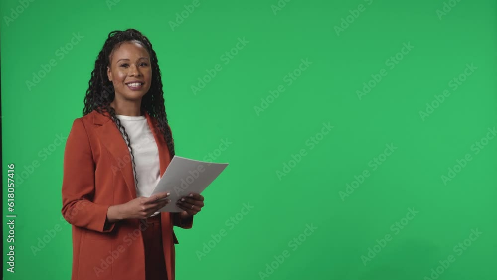 Reporting TV presenter in a studio against a green screen. African American Anchorwoman with a paper in his hands speaks confidently and points to the green screen. Advertising area, workspace mock up Reporting TV presenter in a studio against a green screen. African American Anchorwoman with a paper in his hands speaks confidently and points to the green screen. Advertising area, workspace mock up