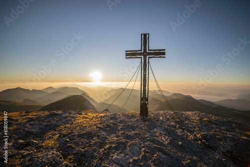 Tranquil scene of a cross on the peak of the Alpine mountain range against a golden sunset sky photo