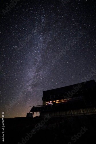 Tranquil night sky illuminated by a bright, milky way backdrop, with a cozy house photo