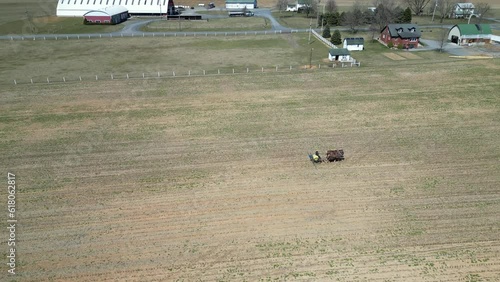 Drone view of a man riding a horse car in a wide farmland with houses and mountain in the background photo