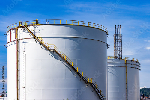 Fototapeta White oil storage fuel tanks at depot station with access ladder against a blue sky