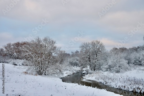 Beautiful calm tranquil winter landscape over the melt river with the bare snow covered trees around