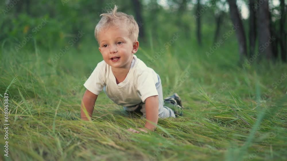 Joyful happy boy crawling in park. First steps. The boy crawls in forest park on the grass. Boy dream concept. The kid takes the first steps in the park on the green grass. Happiness and fun concept Joyful happy boy crawling in park. First steps. The boy crawls in forest park on the grass. Boy dream concept. The kid takes the first steps in the park on the green grass. Happiness and fun concept