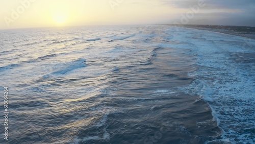 Sunset over ocean waves, flying over the sea during golden hour. Giant waves foaming and splashing in the sea. Drone footage, sunset wavy seascape. Ocean and sky background landscape 