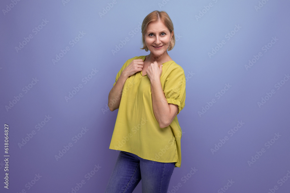 smiling blond mature woman in yellow tank top posing confidently on blue background smiling blond mature woman in yellow tank top posing confidently on blue background