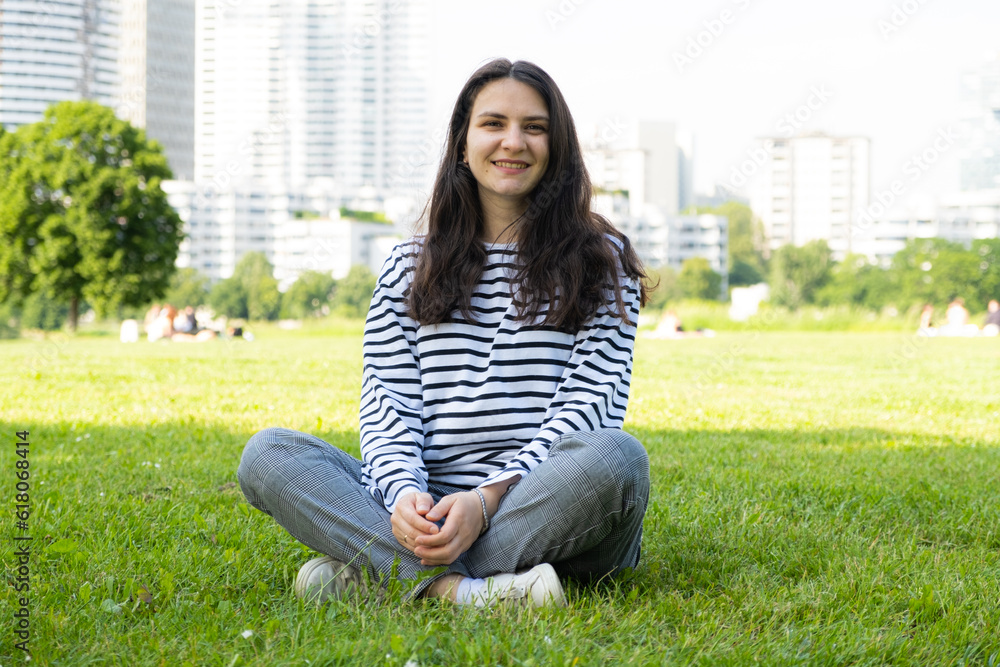 Happy European 30 year old brunette woman sitting on grass in park Happy European 30 year old brunette woman sitting on grass in park