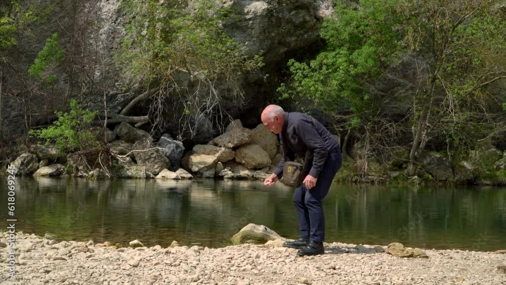 An elderly man collects rocks around a peaceful lake. An elderly man collects rocks around a peaceful lake.