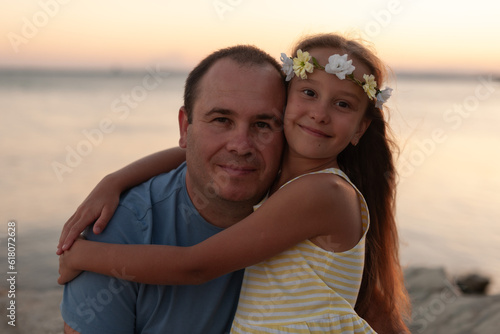 father and daughter  happiness  sea beach  couple  happy father with his cute daughter hugging on the seashore. girl in a yellow dress with a wreath on her head radiating happiness and love.