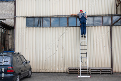 A man high on the stairs dressed in a work uniform mounts the Internet, electricity, fiber optic cable