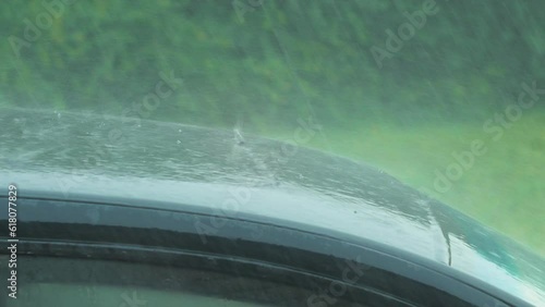 View of heavy storm hail and rain falling on a black car, nature disaster, climate changes, global warming, hot summer day, medium closeup shot photo