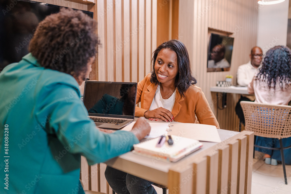 cliente Latina sorrindo discutindo com sua gerente de conta os termos de seu contrato de financiamento bancário em um banco no Brasil cliente Latina sorrindo discutindo com sua gerente de conta os termos de seu contrato de financiamento bancário em um banco no Brasil