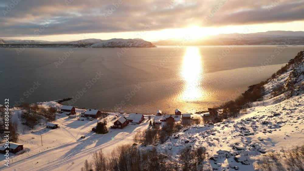 Aerial video of buildings on the rocky sea shore covered with snow during sunset Aerial video of buildings on the rocky sea shore covered with snow during sunset