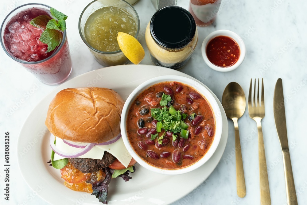Close-up of a hamburger, soup with beans, and refreshing drinks on a table