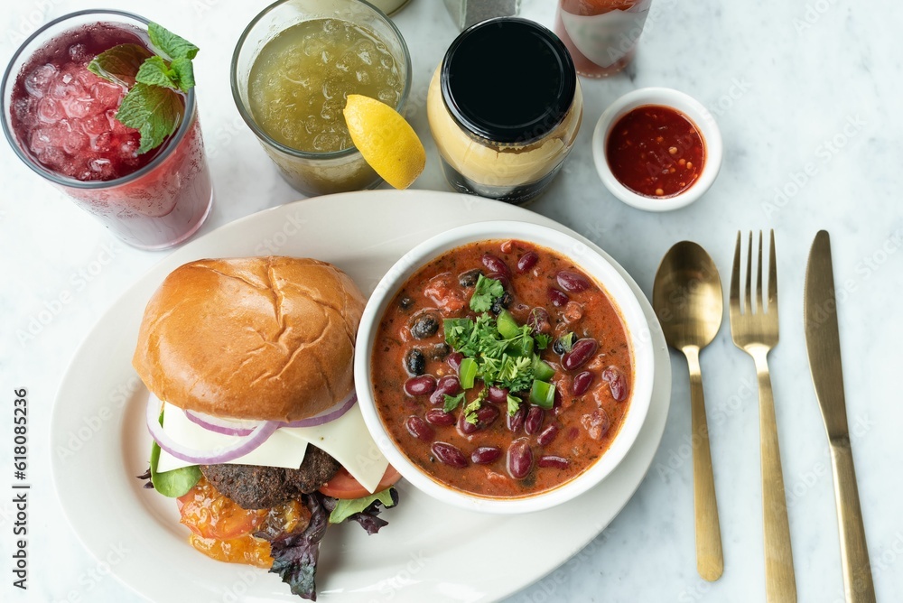 Close-up of a hamburger, soup with beans, and refreshing drinks on a table Close-up of a hamburger, soup with beans, and refreshing drinks on a table
