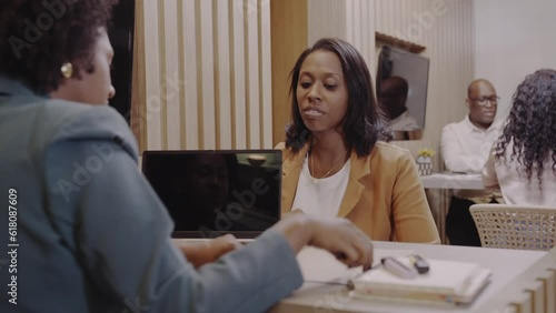 Brazilian bank manager greeting client with handshake and handing over bank loan agreement for her to sign photo