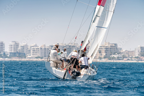 Yacht with crew during regatta in the sea with city on the horizon