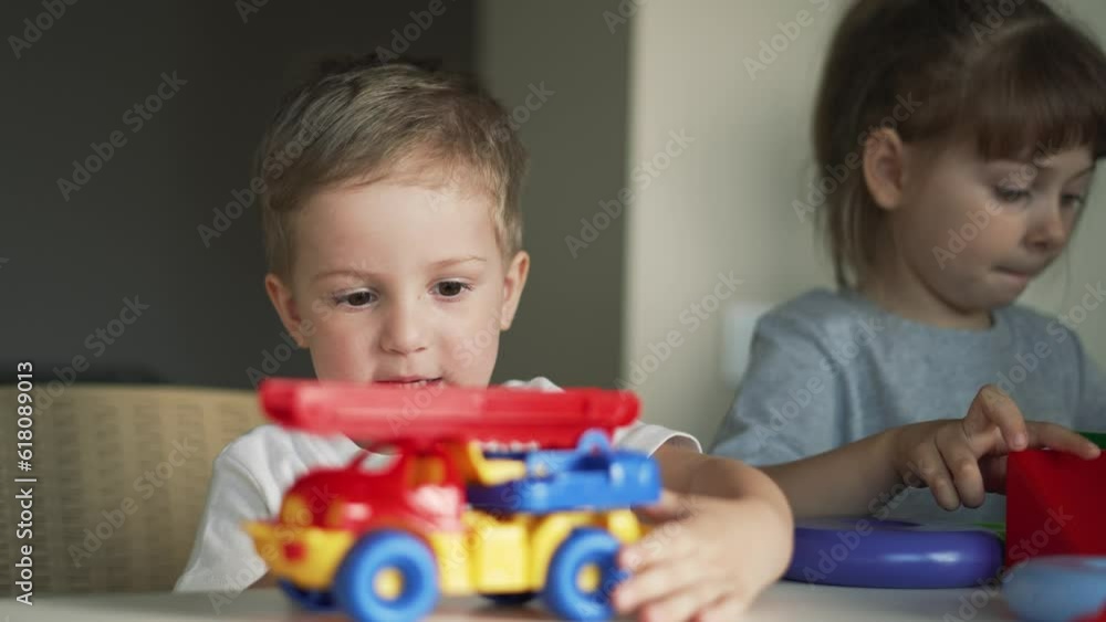 Happy family. Puzzle game. Colored toy in the hands of children. Teaching children in kindergarten. Boys and girls teamwork build cubes. Colored blocks and toy car on table in kindergarten. Schooling Happy family. Puzzle game. Colored toy in the hands of children. Teaching children in kindergarten. Boys and girls teamwork build cubes. Colored blocks and toy car on table in kindergarten. Schooling