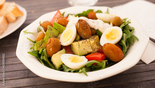 fresh salad of arugula, avocado, cherry tomatoes with olives and quail eggs in white bowl