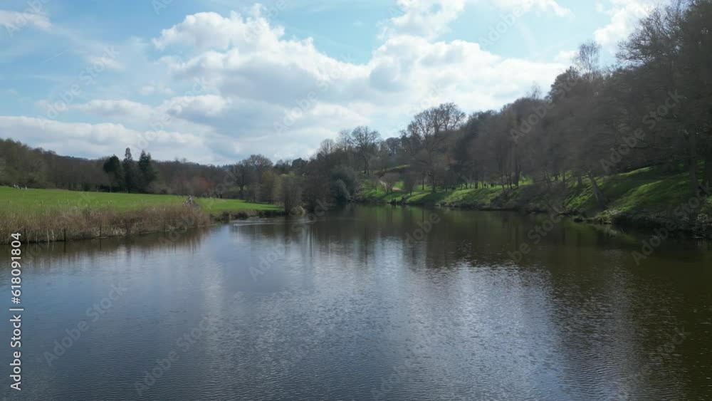 Aerial of a narrow water canal passing alongside the green fields and trees Aerial of a narrow water canal passing alongside the green fields and trees