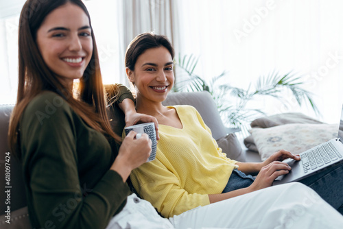 Two happy beautiful women doing a video call sitting on the couch at home.